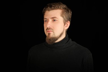 Sevimli sakallı adam, yarım portre, siyah arkaplan. Siyah polo yakalı genç adam. Kendinden emin, başarılı bir adam..