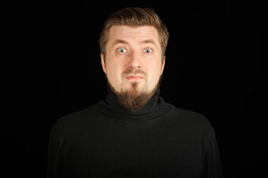 Siyah arka planda sakallı, şaşırmış bir adam. Siyah polo yakalı genç adam. Komik ve tuhaf bir adam..