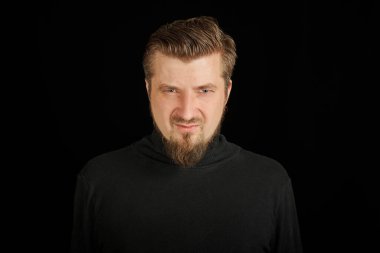 Gergin sakallı adam, siyah arkaplan. Siyah polo yakalı genç adam. Şüpheli ve öfkeli bir adam..