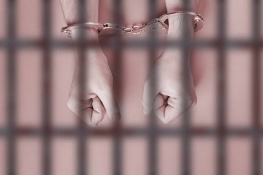 Elleri kelepçeli, parmaklıkların arkasında. Hapsedilme konsepti. Özgürlükten mahrum olmak ve failleri tutuklamak. Yumruklar.