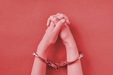 Kırmızı arka planda elleri kelepçeli çapraz eller. Müebbet hapis konsepti. Özgürlükten mahrum bırakma ve failleri yakalama.