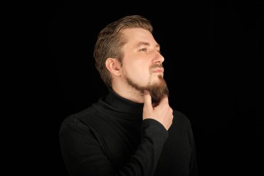 Düşünceli sakallı adam, yarım portre, siyah arka plan. Siyah polo yakalı genç adam. Düşünen ve düşünen başarılı adam..
