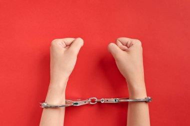 Eller kelepçeli, kırmızı arka planda. Hapsedilme konsepti. Özgürlükten mahrum olmak ve failleri tutuklamak. Yumruklar.