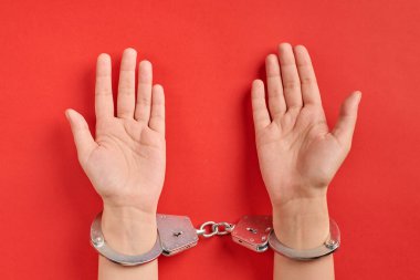 Eller kelepçeli, kırmızı arka planda. Avuçlar yukarı. Müebbet hapis konsepti. Özgürlükten mahrum bırakma ve failleri yakalama.