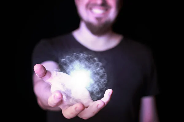 Energy ball in wizard hand. Bearded man casting bright magic ball spell. Black background