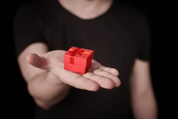 Red gift box in hand. Valentine gift. Small anniversary giftbox from man. Little surprise concept. Black background.