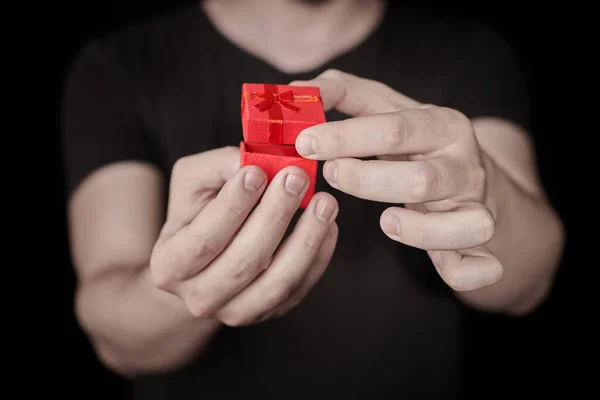 Man give a gift in red gift box. Opening Valentine gift. Small anniversary giftbox from man. Little surprise concept. Black background.