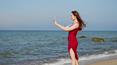 Uzun kahverengi saçlı genç bir kadın, Baltık Denizi kıyısındaki Sandy Plajı 'nda duruyor ve berrak gökyüzünün altında sakin bir suya bakıyor. Sahne, sükuneti ve düşünmeyi yumuşak doğal ışıklandırmayla iletir.