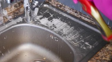 Paslanmaz çelik mutfak lavabosu köpük ve akan suyla eksiksiz temizlik görüyor. Yakın plan görüntüsü, parlak ışıklandırma altında döşeme arkaplanı temizleme eylemini yakalar