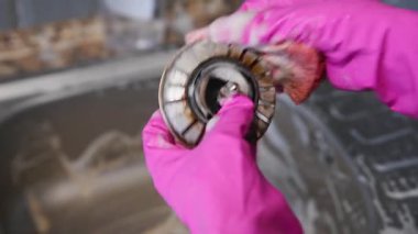 Parlak pembe eldivenler giyen, mutfak lavabosu giderini sabunlu köpükle ovalayan ellerin yakın çekimi. Doğal ışık paslanmaz çelik lavaboyu ve granit tezgahı ön plana çıkarıyor