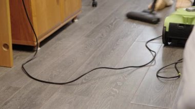 Yumuşak ışıklandırmalı sıcak odada ahşap zemini temizleyen yeşil elektrikli süpürgeye yakın plan. Bulanık arkaplan elementlerine ve vakum gövdesine odaklan