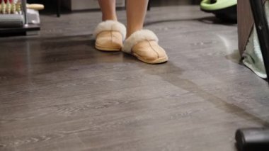 Evin içinde terlik giyen, temiz, koyu renk ahşap döşeme giyen biri. Yumuşak ışıklandırma, düşük perspektiften zemin dokusunu vurgular