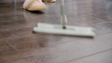 Koyu ahşap zemin mikrofiber paspas kullanılarak temizleniyor. Kapalı alanda ışıklandırma cilalanmış yüzey dokusu ve parlaklığını vurgular