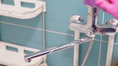 Krom musluk banyoda temizleniyor açık mavi fayanslar ve beyaz raflar var. Resim, parlak ışık altında musluktaki su damlacıklarını yakalar