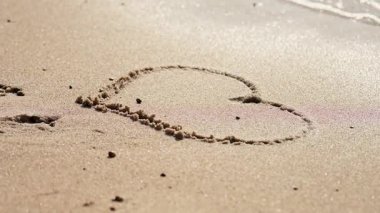 Parlak güneş ışığı altında pürüzsüz kumlu kıyılara kazınmış pürüzsüz kalp şekli yumuşak, köpüklü plaj yüzeyini terk ederek bembeyaz deniz köpüğü gibi eriyip gider.