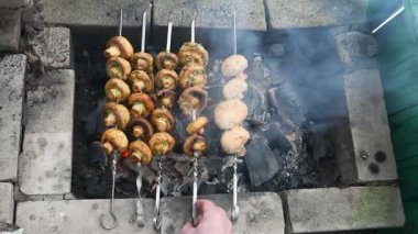 Metal şişler üzerine dizilmiş mantar kebabı, taşralı mangal çukurunda kızgın kömürün üzerinde ızgara yapıyor. Duman şişlerin etrafında yükselir, açık havada zengin, dumanlı bir atmosfer yaratır.