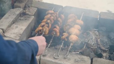 Mantar kebabının açık hava taş ızgarasında sıcak kömür yüzünden metal şişler üzerinde kızardığı yakın çekim görüntüsü. Yükselen dumanların arasında şişleri ayarlayan eller kırsal aşçılık ortamını yakalıyor