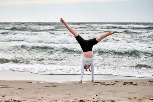 Açık renk saçlı genç bir kadın Baltık Denizi sahilinde takla atıyor. Bulutlu gökyüzü, dinamik hareketi çarptıran dalgalar, dingin arka planla çelişiyor. Enerjik, zarif bir an.