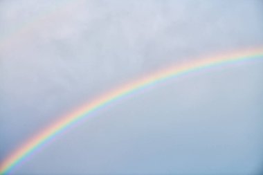 Narin gökkuşağı zarif bir şekilde soluk mavi gökyüzü boyunca uzanır, ince bulut oluşumlarıyla, huzur verici ve canlandırıcı doğal bir sahne yaratır.