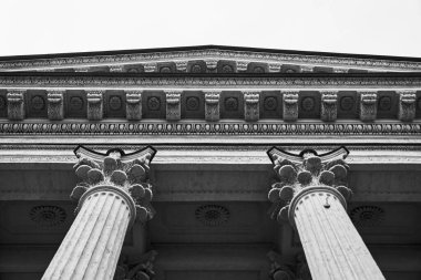 Korint sütunları ve süslemeleri içeren düşük açılı siyah beyaz fotoğraf, karmaşık taş işçiliği ve tarihi mimari tasarımı vurguluyor.