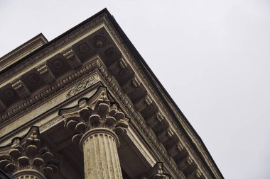 Klasik korint sütununa yakın perspektif ayrıntılı büyük harfleri ve tabloları, nötr gökyüzü arka planıyla dağınık, yumuşak gün ışığı altında sergiliyor.