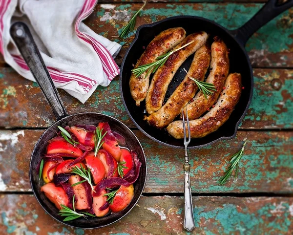 Frites saucisses aux pommes, oignons et romarin dans une poêle à frire苹果、 洋葱和迷迭香在平锅里煎炸的香肠 — 图库照片