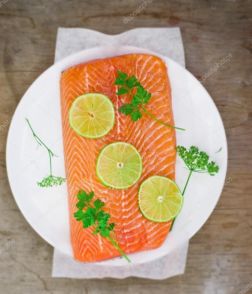 fresh, crude fillet of a salmon with slices of a lime and greens 
