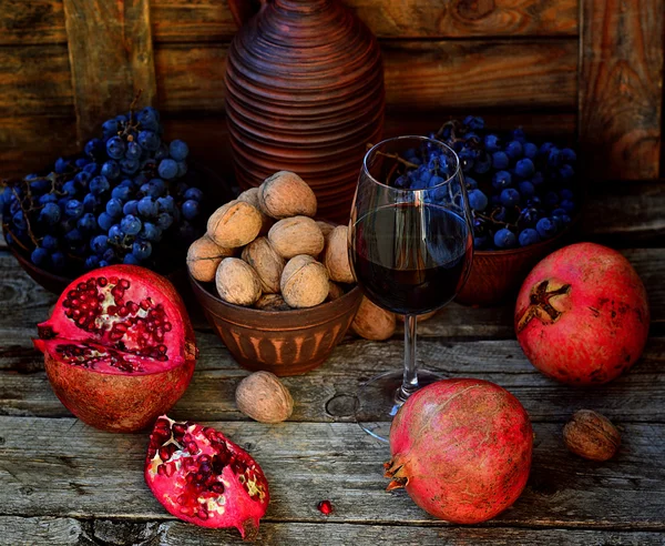 Melograno, noci e bicchiere di vino su fondo di legno — Foto Stock