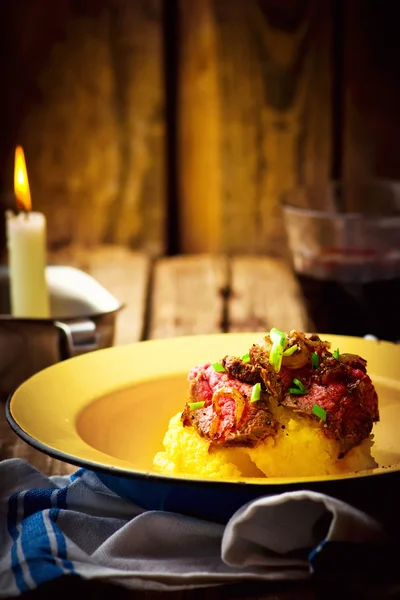 Gebraden rundvlees en polenta in een ijzeren kom op een houten tafel. — Stockfoto