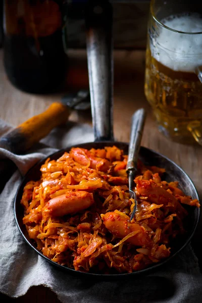 Stewed cabbage with sausages in a vintage frying pan and a mug with beer. — Stock Photo, Image