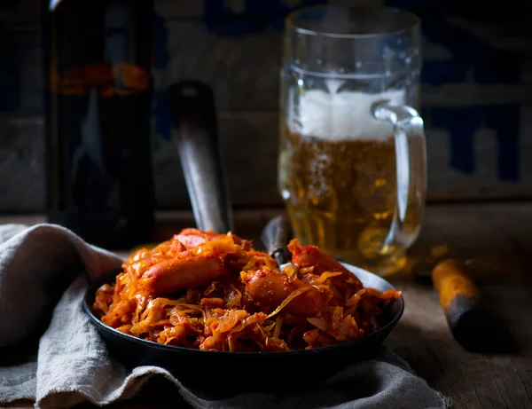 vintage bir kızartma tavası ve bir kupa bira ile sosis ile haşlanmış lahana.