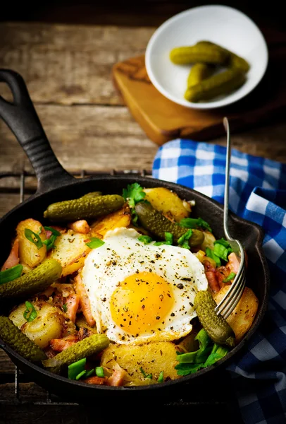 Country breakfast from potatoes, with bacon and fried eggs in a pig-iron frying pan. — Stock Photo, Image