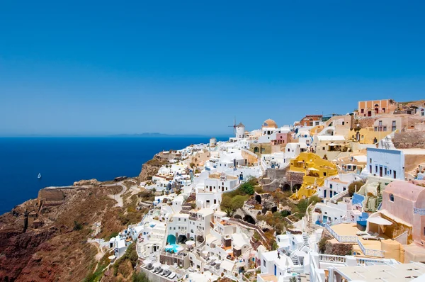 Kolorowe miejscowości Oia na skraju klifów caldera z wiatrakami w oddali na wyspy Thira (Santorini), Grecja. — Zdjęcie stockowe