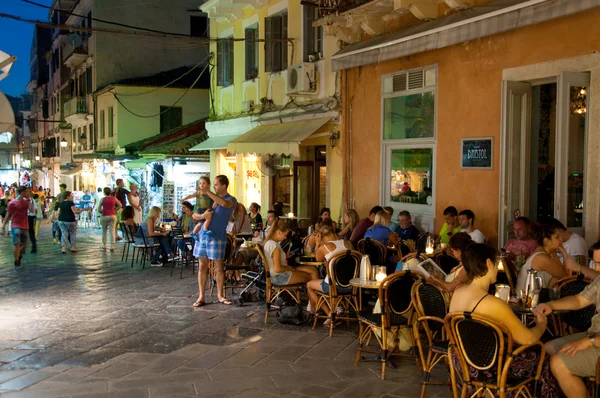 CORFU-25 DE AGOSTO: Los turistas cenan en un restaurante local el 25 de agosto de 2014 en la ciudad de Kerkyra en la isla de Corfú, Grecia. Kerkyra es una ciudad en la isla de Corfú en el mar Jónico, Grecia. . —  Fotos de Stock