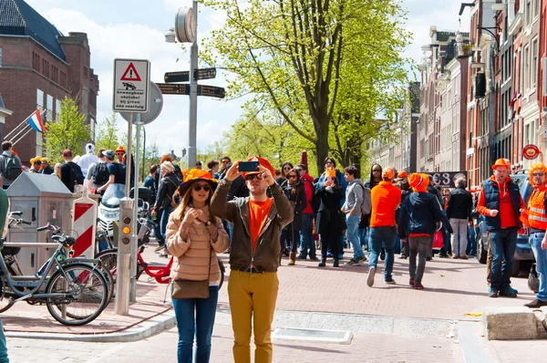 Amsterdam, Nederland-27 April: Jong koppel in oranje nemen foto rond wallen op Konings dag op April 27,27 in Amsterdam. — Stockfoto