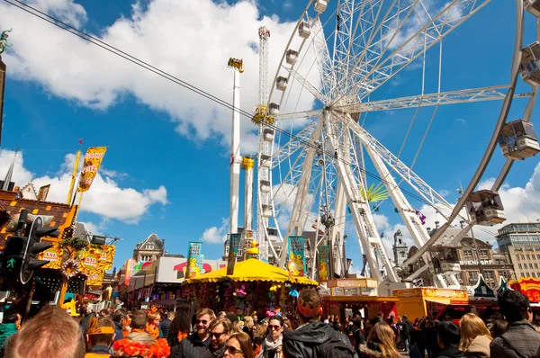 AMSTERDÃO, PAÍSES BAIXOS-ABRIL 27: Dia do Rei na Praça da Barragem com parque de diversões e pessoas vestidas de laranja em abril 27.2015 em Amsterdã . — Fotografia de Stock