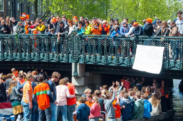 AMSTERDAM,NETHERLANDS-APRIL 27: Boat paty on the Singel canal, crowd of people on the bridge on King's Day on April 27,2015. — Stockfoto