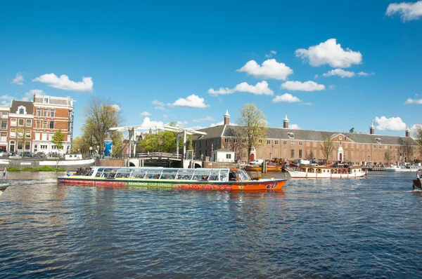 Amsterdam paesaggio urbano, i turisti godono di crociera sul canale, Magere Brug (Ponte Magro) e Hermitage Amsterdam sono visibili sullo sfondo, Paesi Bassi . — Foto Stock