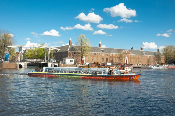 Amsterdam paesaggio urbano, i turisti godono di crociera sul canale, Magere Brug noto anche come Skinny Bridge e Hermitage Amsterdam sono visibili sullo sfondo, Paesi Bassi . — Foto Stock