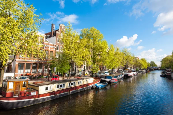 Amsterdam canal con barcos a lo largo de la orilla del río . Fotos de stock libres de derechos