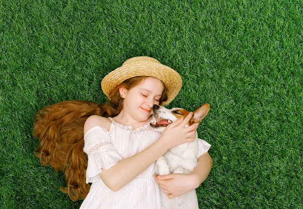 Cute girl and dog hugging, kissing  and lying on the green grass in the spring park. Spring, Easter, friends concept.