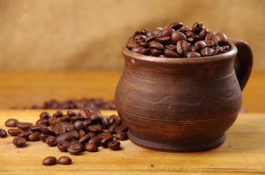 ahşap bir masa üzerinde bir kil fincan kahve çekirdekleri