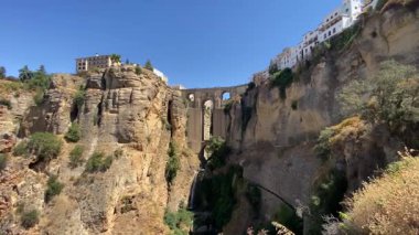 Ronda, İspanya. 31 Ağustos 2025. El Tajo vadisi ve İspanya 'nın Ronda kentindeki Puente Nuevo köprüsünün alçak açılı manzarası açık mavi bir yaz gökyüzüne karşıdır..