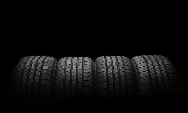 Quatre pneus en caoutchouc automobile isolés sur fond noir — Photo