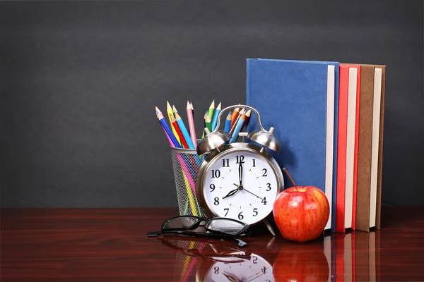 Libros, manzana, despertador y lápices en mesa de escritorio de madera y bla —  Fotos de Stock