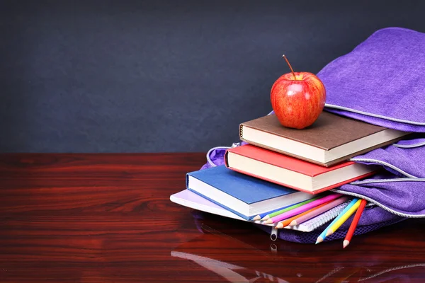 Libros, manzana, mochila y lápices en mesa de escritorio de madera y negro —  Fotos de Stock