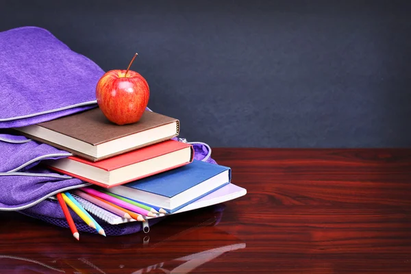 Libros, manzana, mochila y lápices en mesa de escritorio de madera y negro —  Fotos de Stock