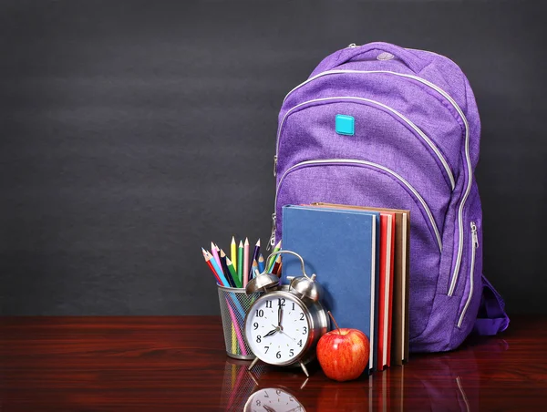 Books, apple, backpack, alarm clock and pencils on wood desk tab — Stock Photo, Image