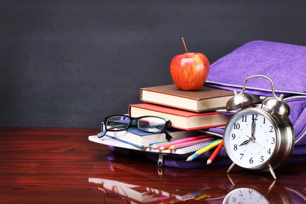 Books, apple, backpack, alarm clock and pencils on wood desk tab — Stock Photo, Image