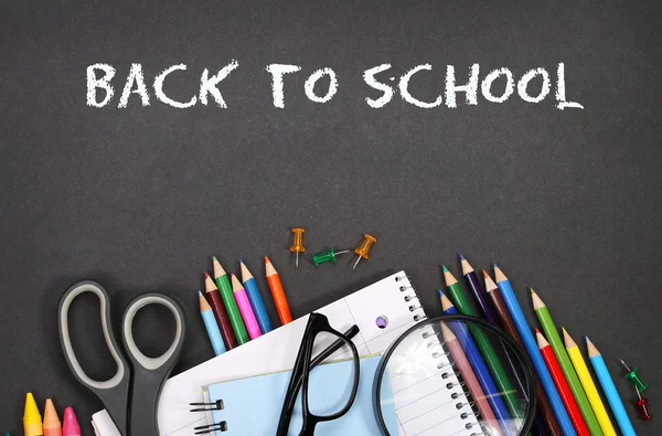 Notebook, exercise book, scissors and pencils on black board bac — Stock Photo, Image